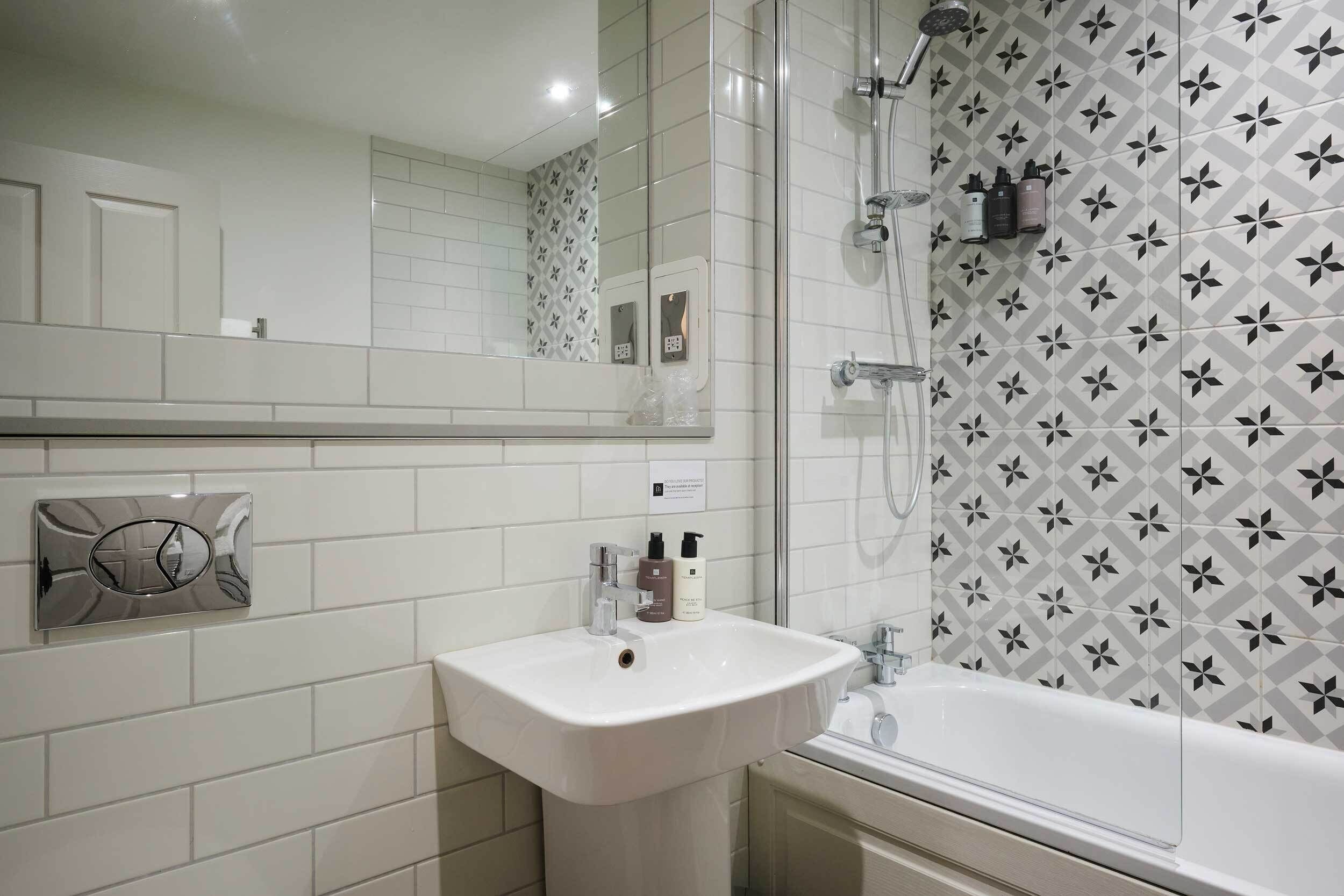 A bathroom with a white sink, a mirror, a shower with a glass door, and a patterned wall.
