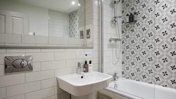 Un bagno con un lavandino bianco, uno specchio, una doccia con porta in vetro e una parete decorata.