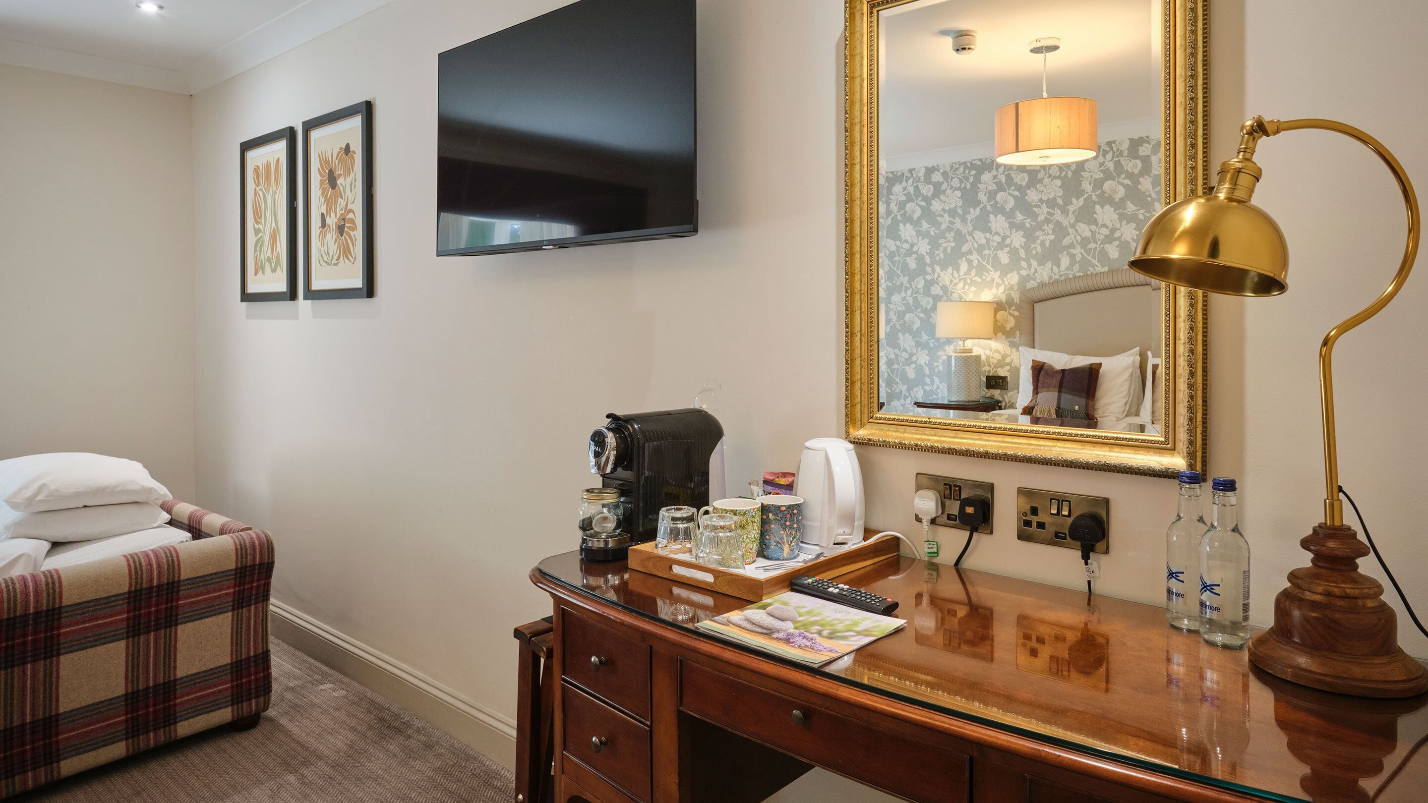 Una habitación de hotel con una cama, un escritorio con lámpara, un televisor y un espejo.