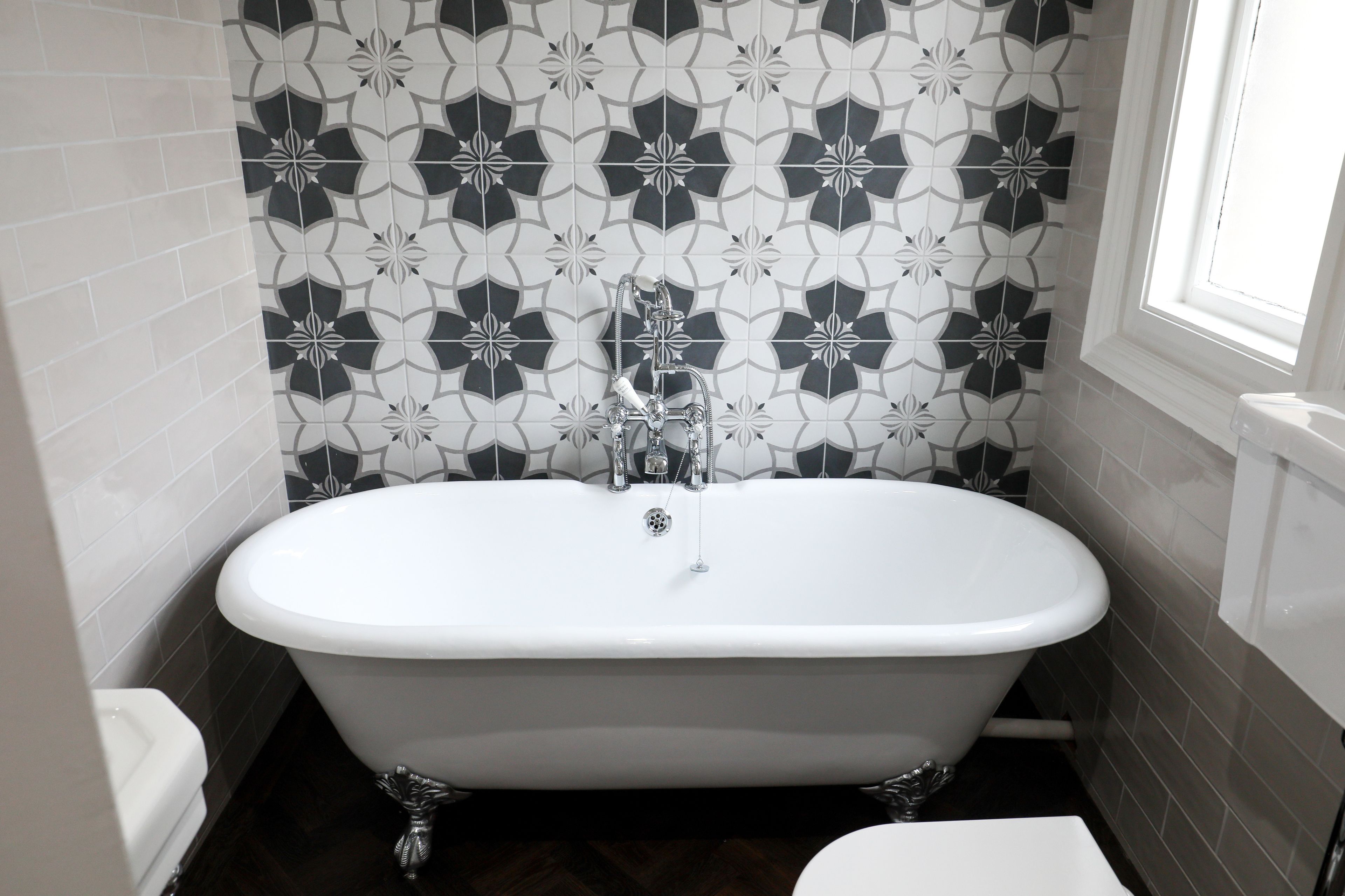 A bathroom with a freestanding bathtub, white tiles, and a window.