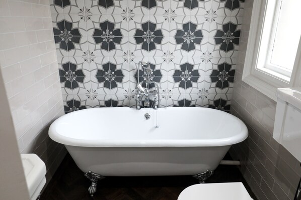 A bathroom with a freestanding bathtub, white tiles, and a window.