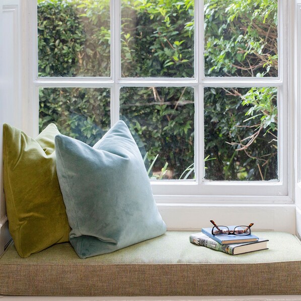 A window seat with cushions, a book, and glasses.