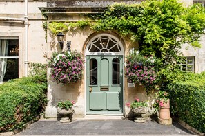 Una porta verde con arco decorativo, circondata da vegetazione lussureggiante e vasi fioriti.