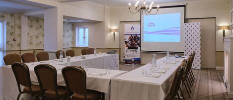 A conference room with a long table, chairs, a projector screen, and a presentation stand.