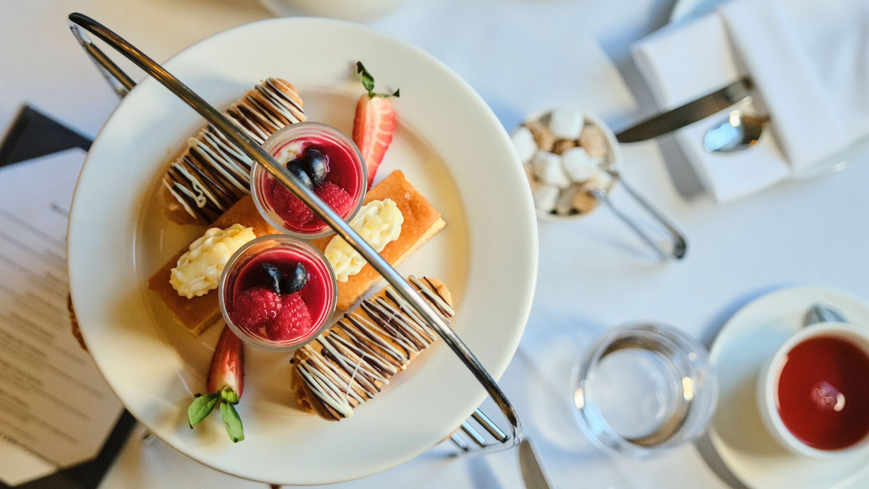 A dessert plate with pastries, berries, and a glass of red beverage on a table.