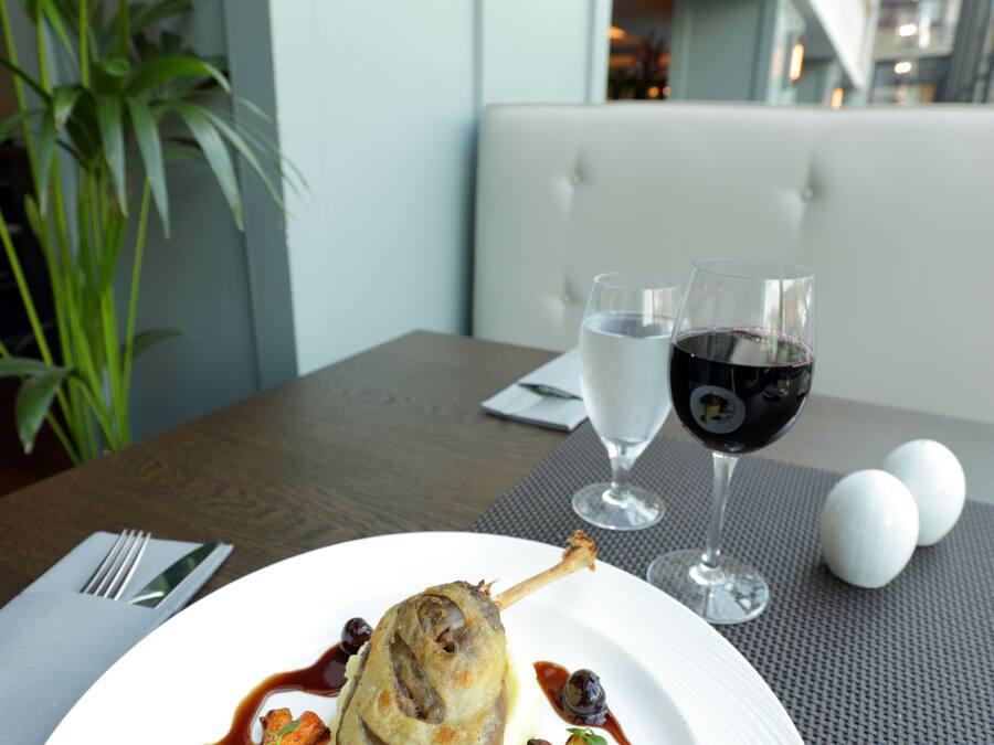 A dining table with a plate of food, two glasses of wine, and a potted plant.