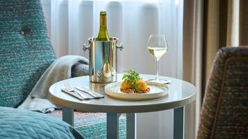 A dining table with a bottle of champagne, a glass of wine, and a plate of food in a hotel room.