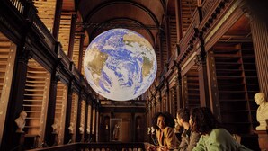 Un vaste intérieur de bibliothèque, orné de boiseries travaillées, abritant un grand globe terrestre et des sculptures classiques.