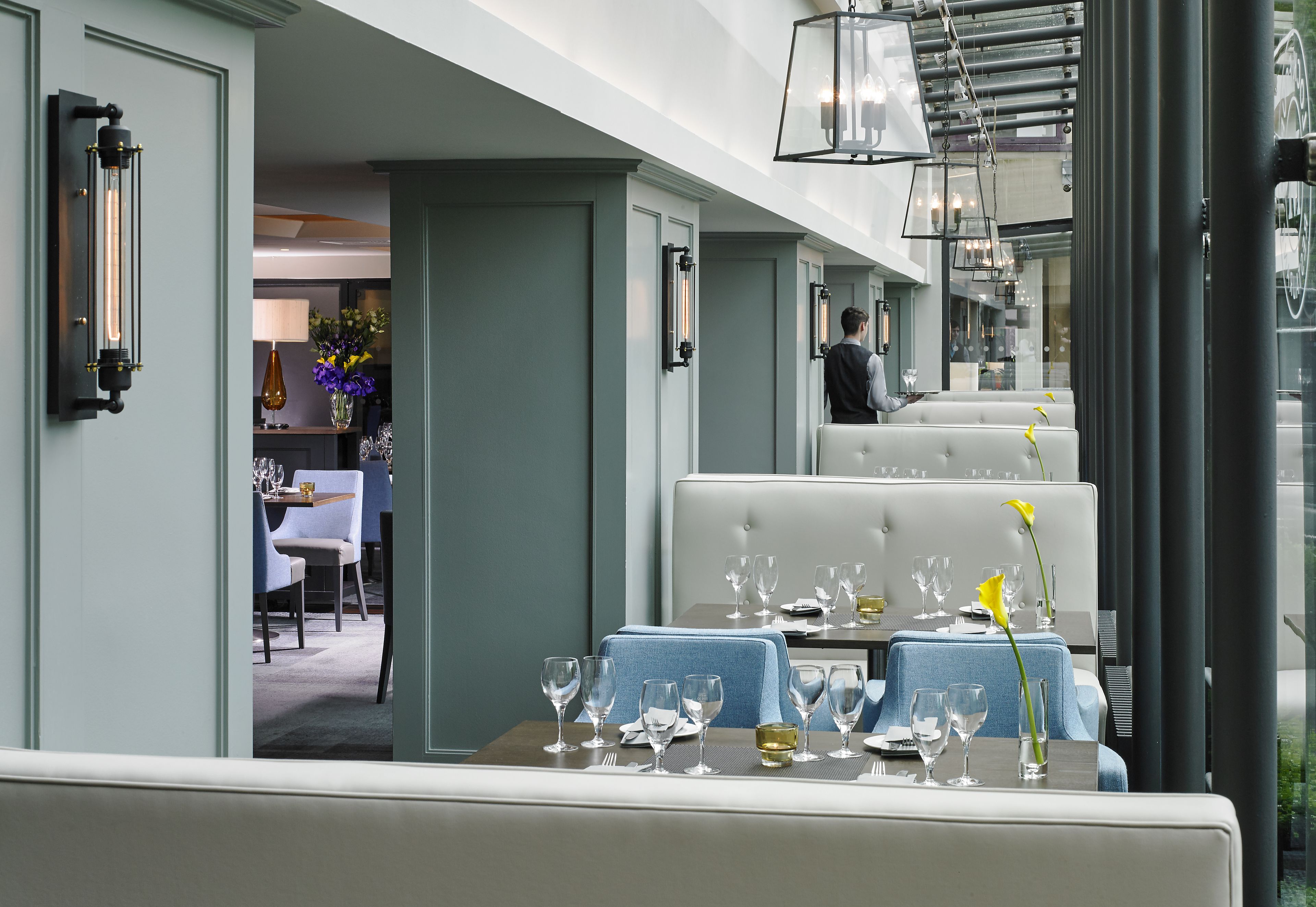 Un comedor con una mesa dispuesta para comer, un camarero al fondo y vista del interior del restaurante.
