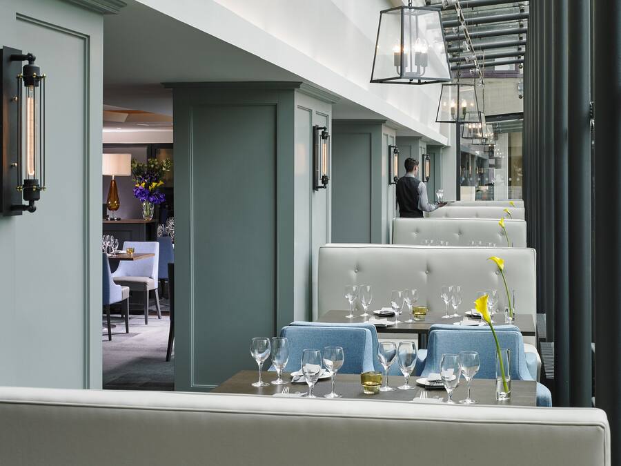 Un comedor con una mesa dispuesta para comer, un camarero al fondo y vista del interior del restaurante.