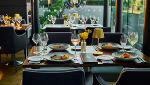 L’intérieur d’un restaurant, avec des tables dressées pour le service, un logo sur le mur et une vue par la fenêtre.