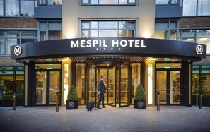 El exterior del Hotel Mespil, con su entrada, y un hombre con traje caminando hacia ella.