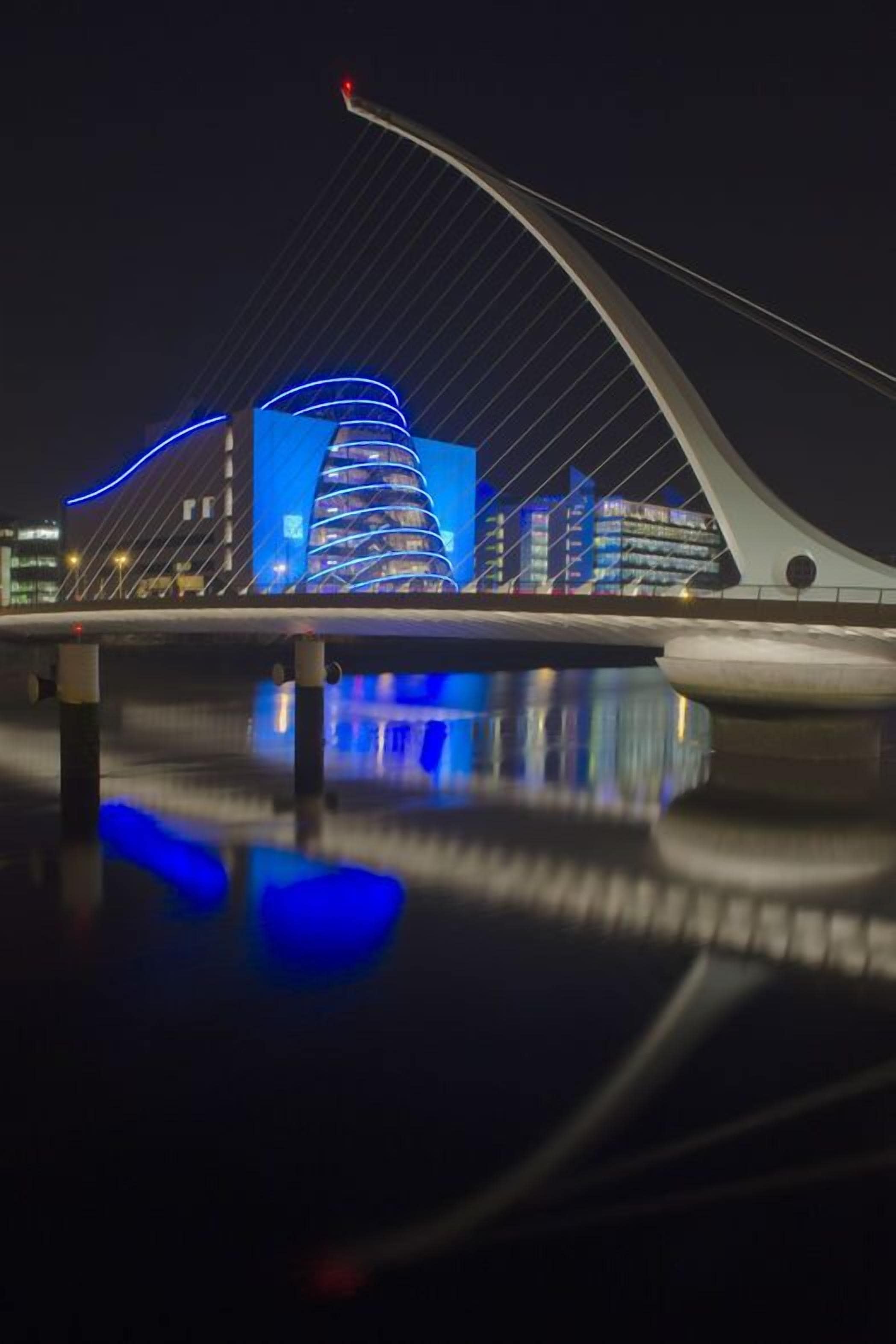 A modern bridge with a unique cable design and illuminated blue lighting, reflecting on the water below.