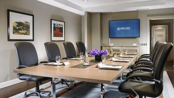 A conference room with a long table, black chairs, a flat-screen TV, and framed artwork on the wall.