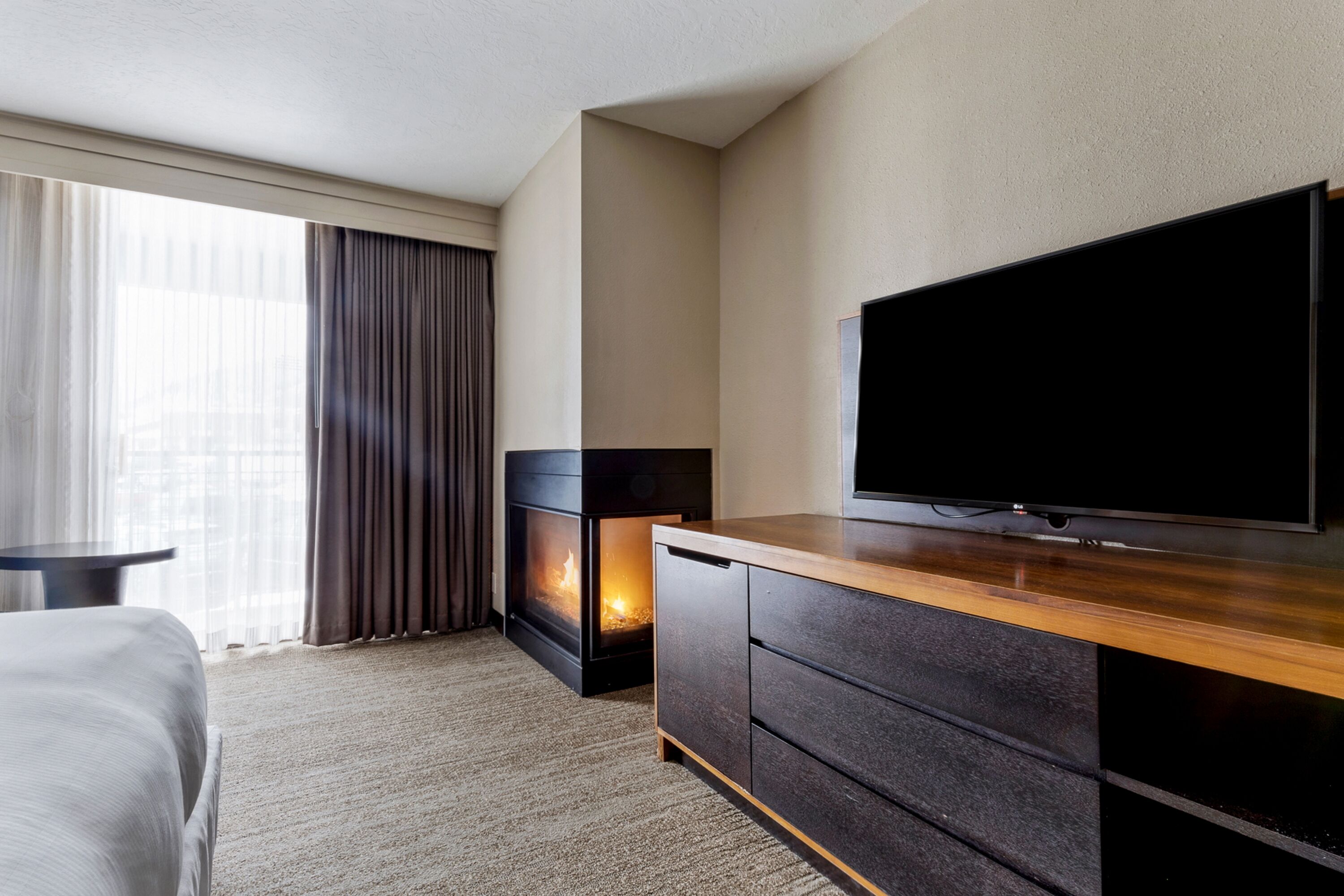 Une chambre d’hôtel dotée d’une grande télévision à écran plat, d’une cheminée, d’un lit et offrant une vue sur la ville grâce à de grandes fenêtres.