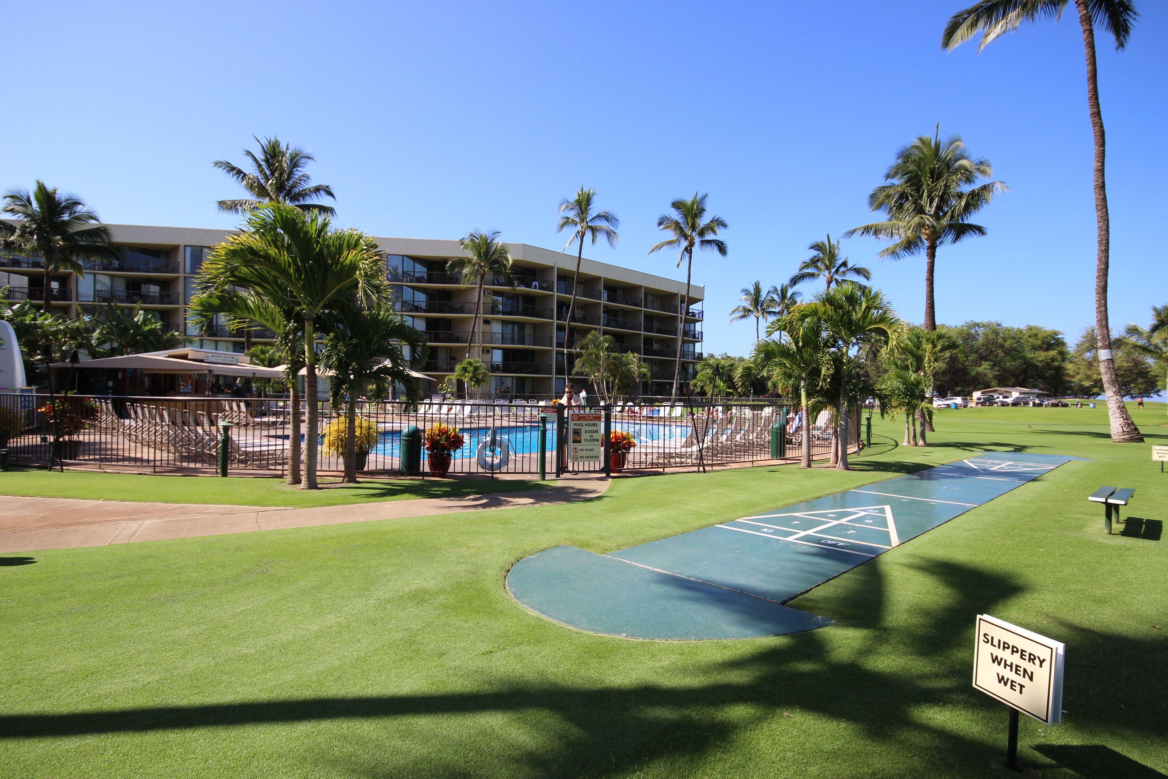 A hotel with a pool area, palm trees, and a sign warning of a slippery surface when wet.