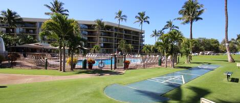 A hotel with a pool area, palm trees, and a sign warning of a slippery surface when wet.