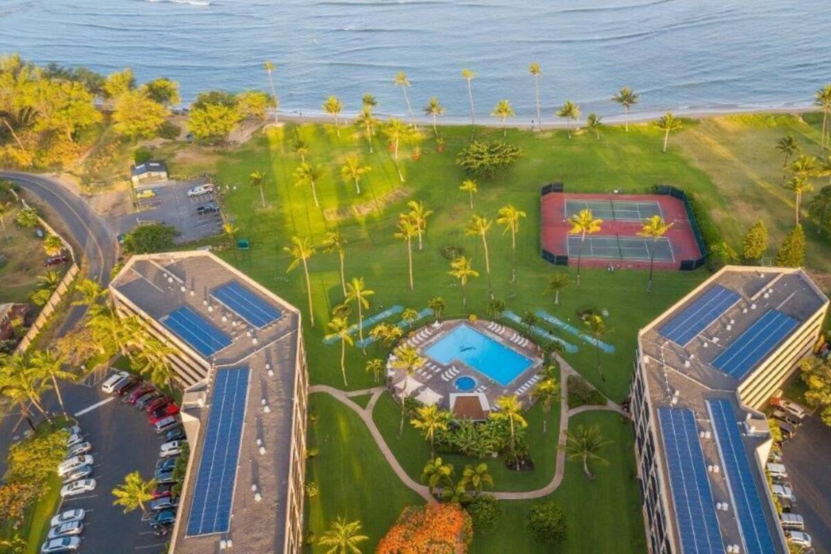 An aerial view of a resort with a central pool, solar panels, and a tennis court.