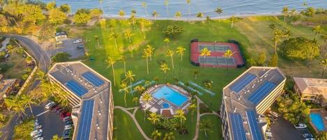 Eine Luftaufnahme eines Resorts mit einem zentralen Pool, Solaranlagen und einem Tennisplatz.