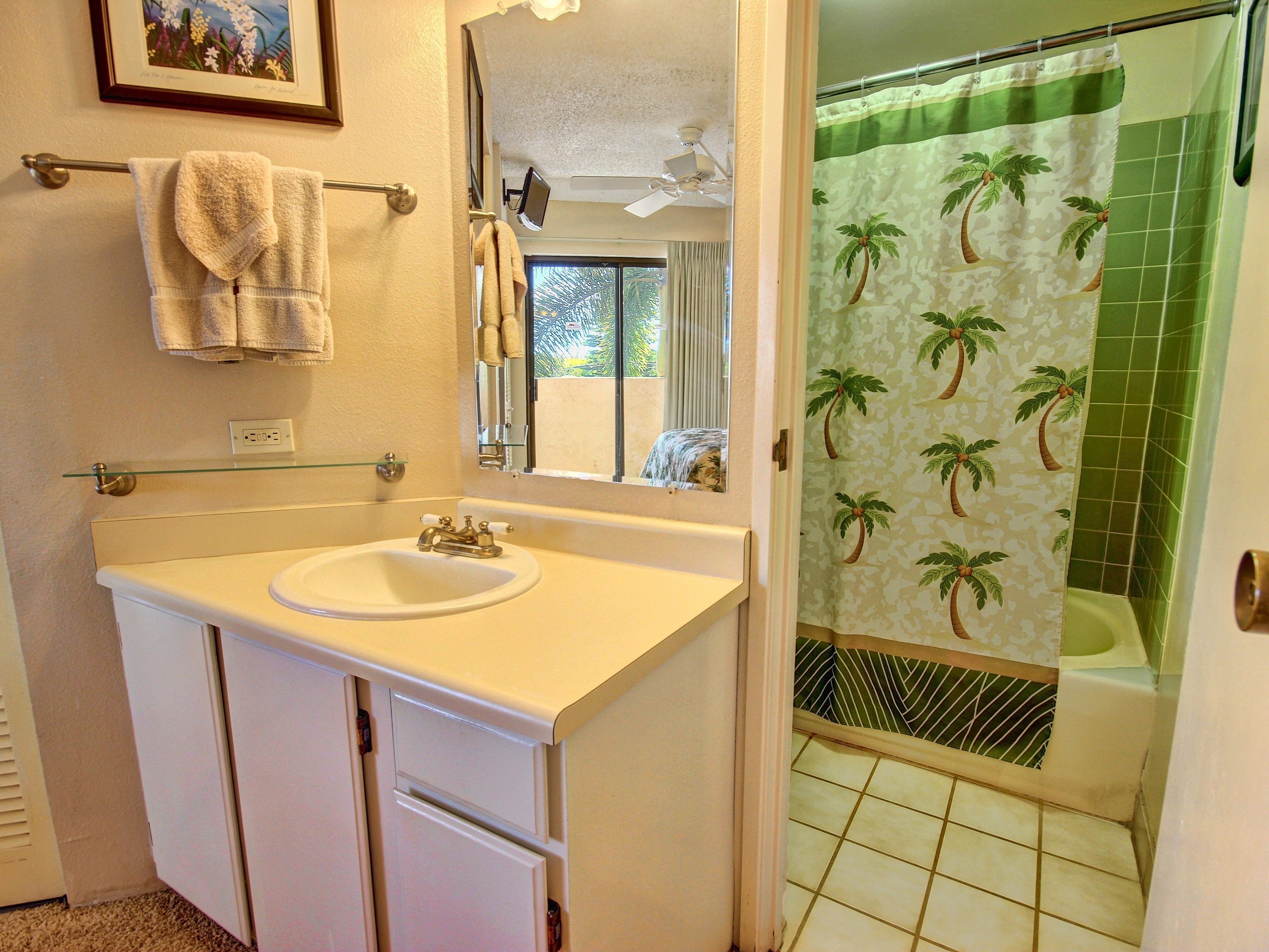A bathroom with a white sink, a mirror, a towel rack, and a shower with a palm tree shower curtain.
