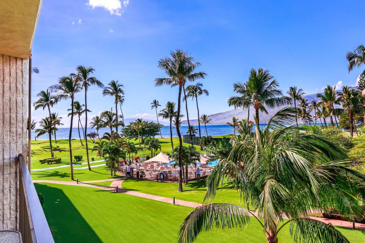 A resort with a well-maintained lawn, palm trees, and a view of the ocean.