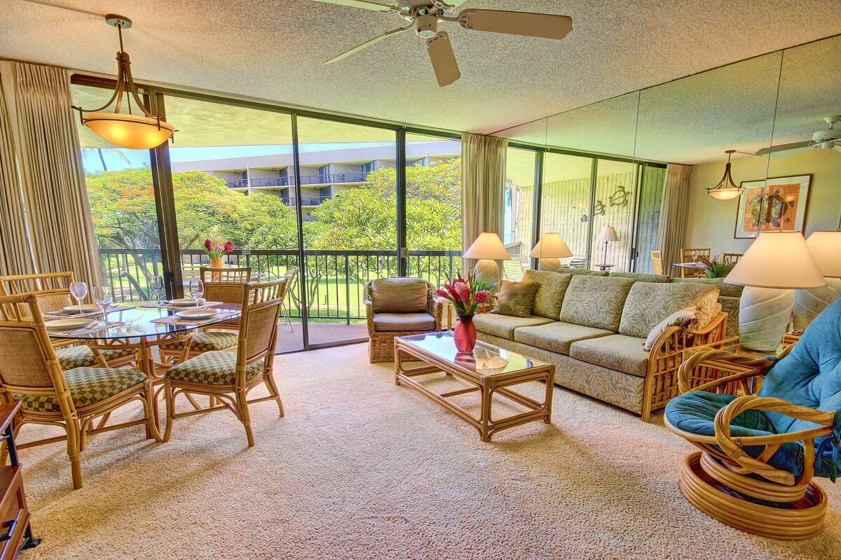A spacious living room with a balcony, furnished with wicker chairs, a sofa, and a coffee table.