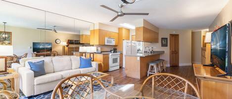 A modern living room with a sofa, chairs, a dining table, and a kitchen area with appliances.