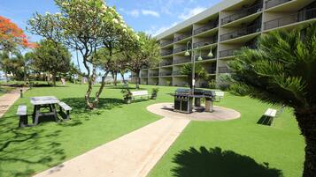 A courtyard with a barbecue area, picnic tables, and a pathway leading to a building with balconies.