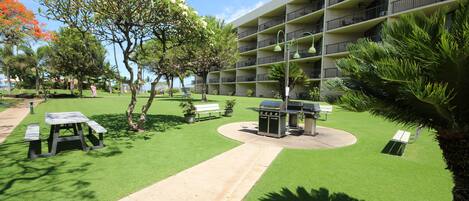 A courtyard with a barbecue area, picnic tables, and a pathway leading to a building with balconies.