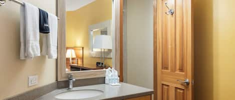 Une salle de bain avec un lavabo, un miroir, un porte-serviettes et une porte en bois.