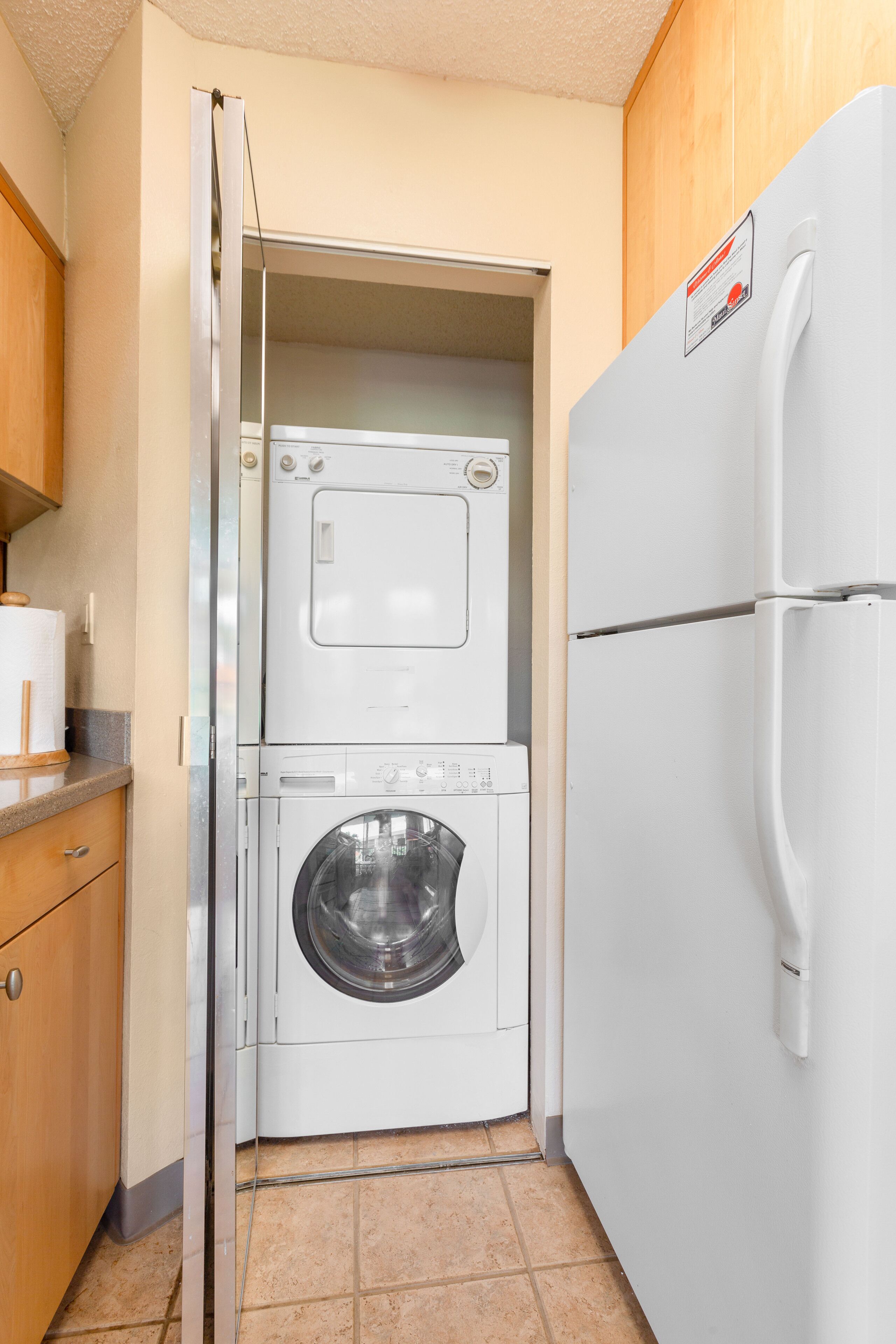 A compact laundry area with a stacked washer and dryer, a white refrigerator, and wooden cabinets.