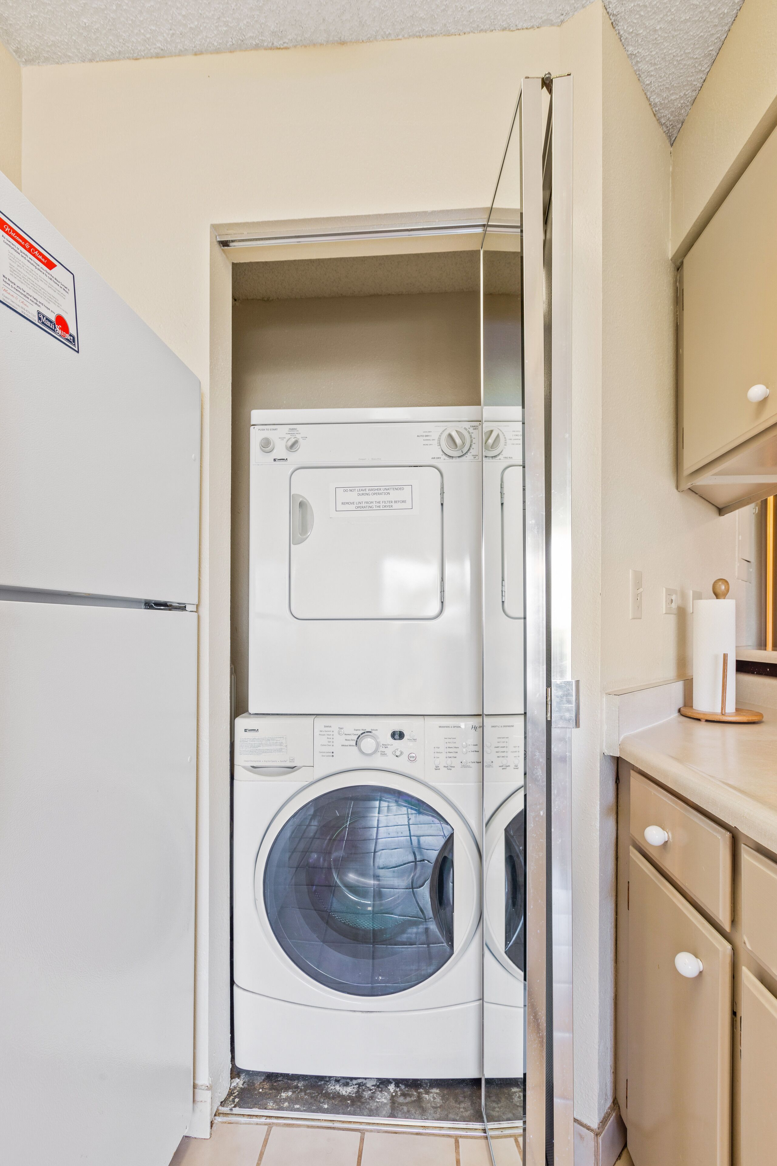 A compact laundry room with a stacked washer and dryer, a small countertop, and a cabinet.
