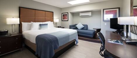Una habitación de hotel con una cama grande, un escritorio, una silla, un sofá y un equipo de aire acondicionado.