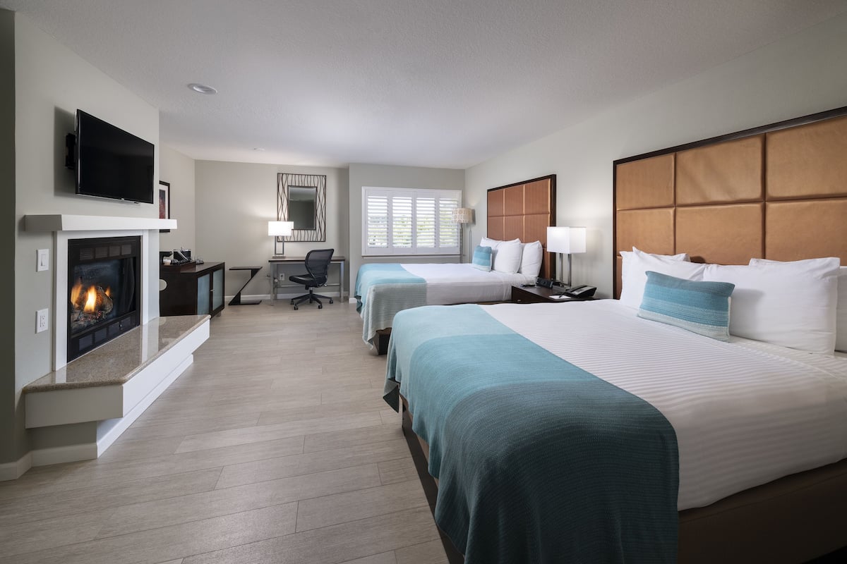 A hotel room with a fireplace, two beds, a desk, and a TV.