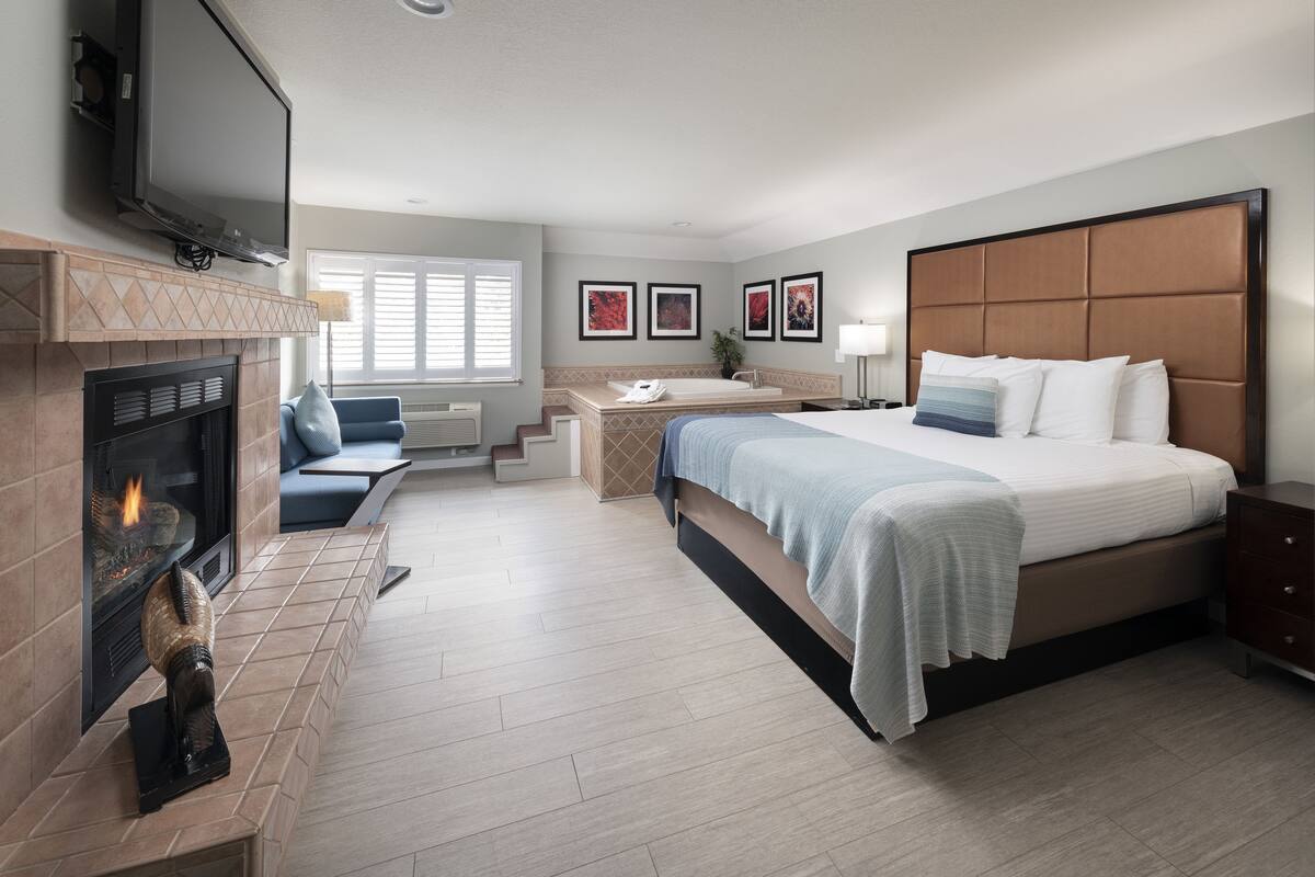 A hotel room with a bed, a fireplace, a TV, a desk, and a bathroom.