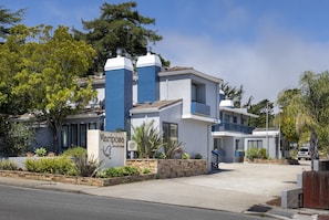 A modern hotel with a blue and white facade, a landscaped front yard, and a clear sky. - Mariposa Inn & Suites (Monterey)