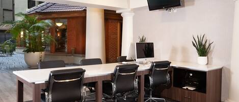 A conference room with a long table, four black chairs, a computer, and a TV mounted on the wall.