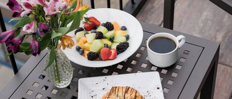 A table with a fruit salad, a cup of coffee, and a pastry.