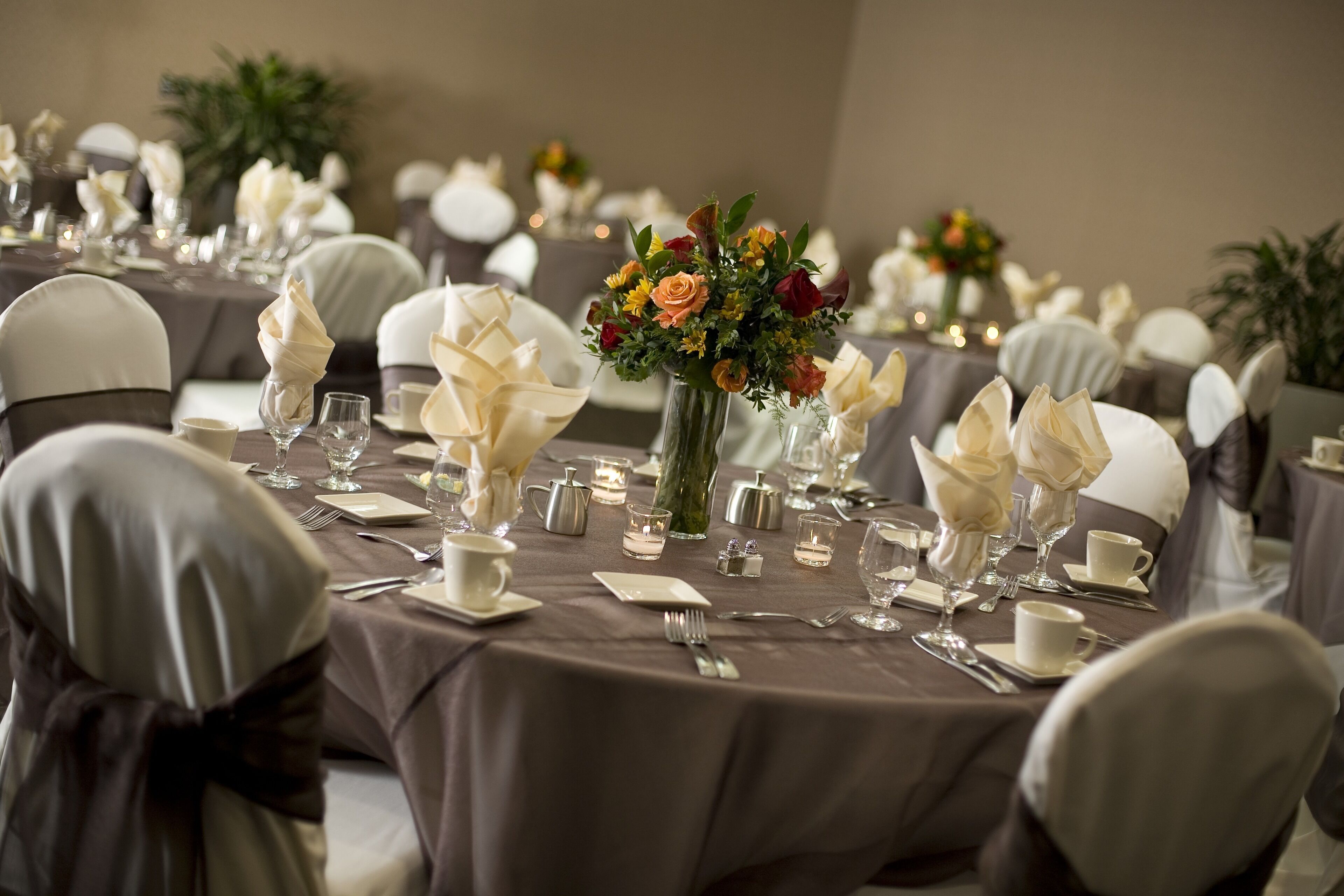 Een balzaal met ronde tafels, gedekt voor een formeel evenement, met witte servetten, glazen en bloemdecoraties.