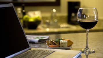 Una laptop, una copa de vino tinto y un plato con queso y galletas sobre una mesa.