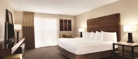 A hotel room with a large bed, a desk, a chair, a TV, and a window with curtains.