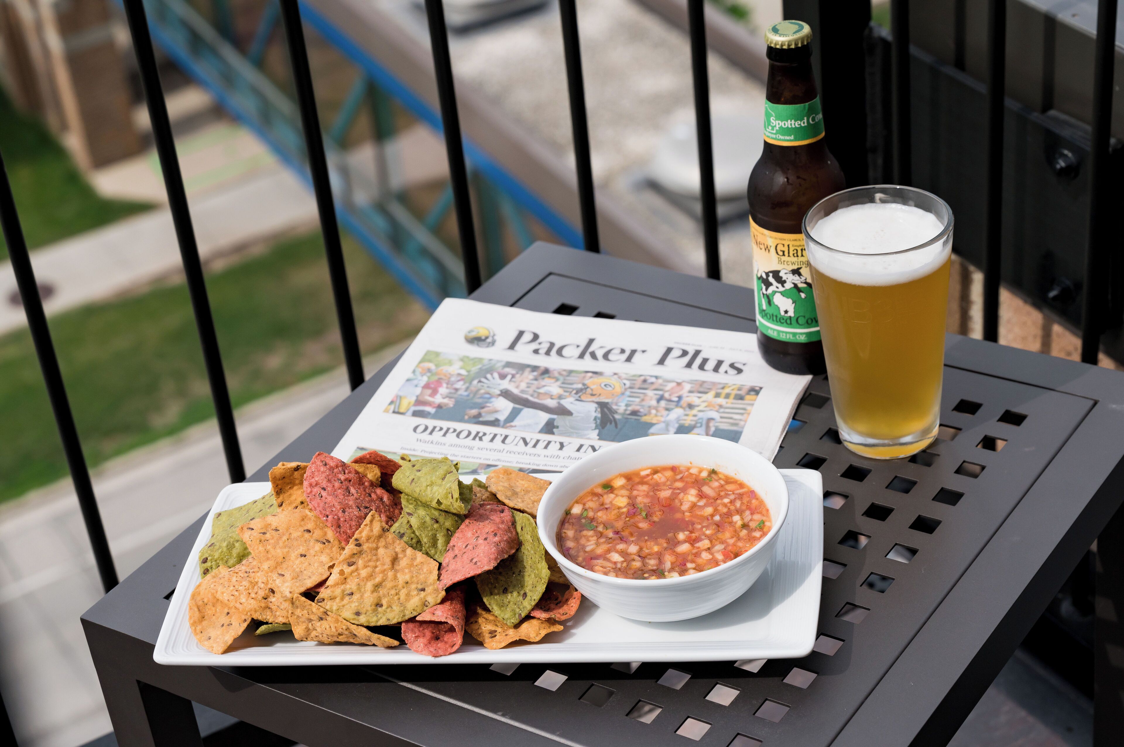Ein Tisch mit Nachos, einer Salsa-Schale, einem Bierglas und einer Bierflasche auf einem Balkon.