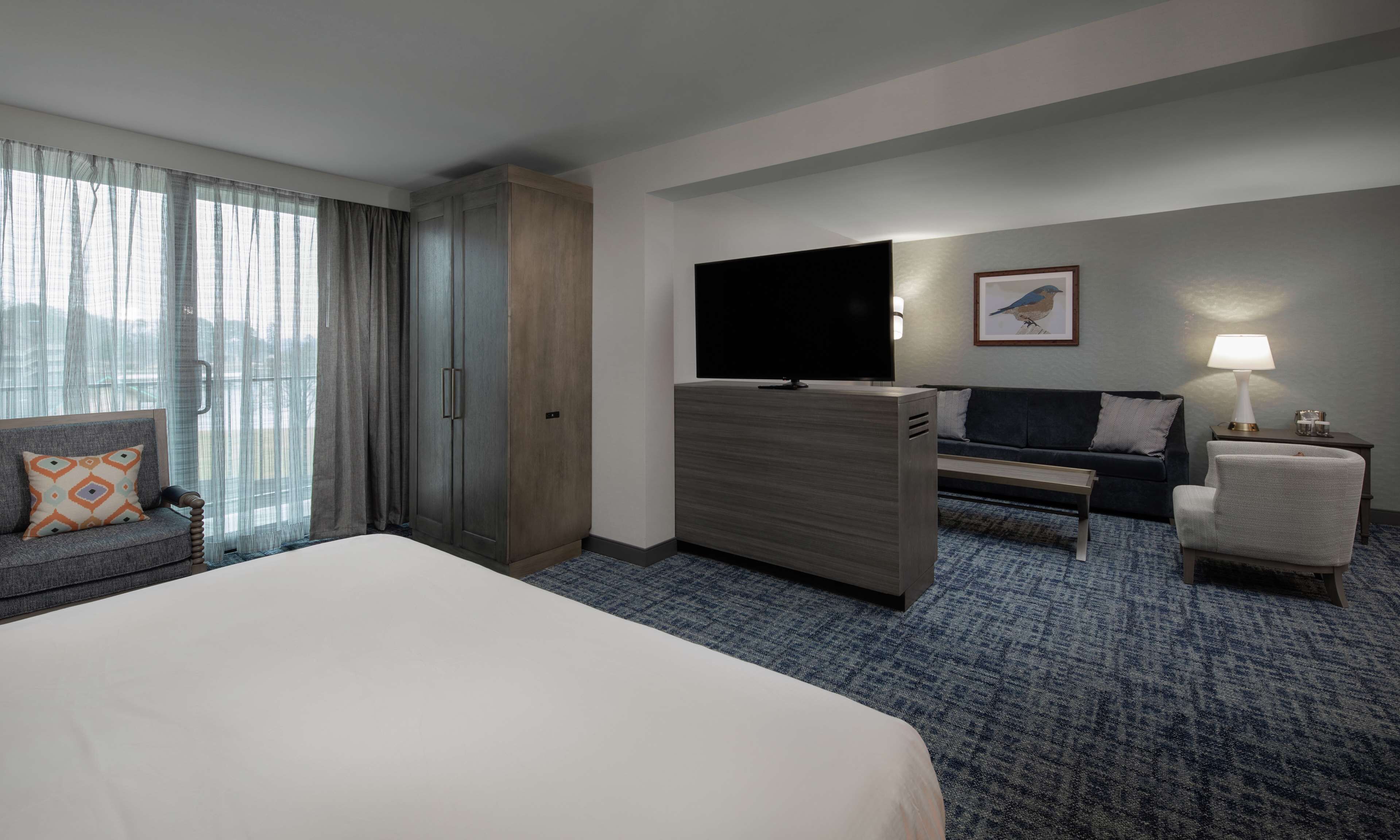 A hotel room with a large bed, a TV, a sofa, a chair, and a desk.