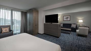 A hotel room with a large bed, a TV, a sofa, a chair, and a desk.