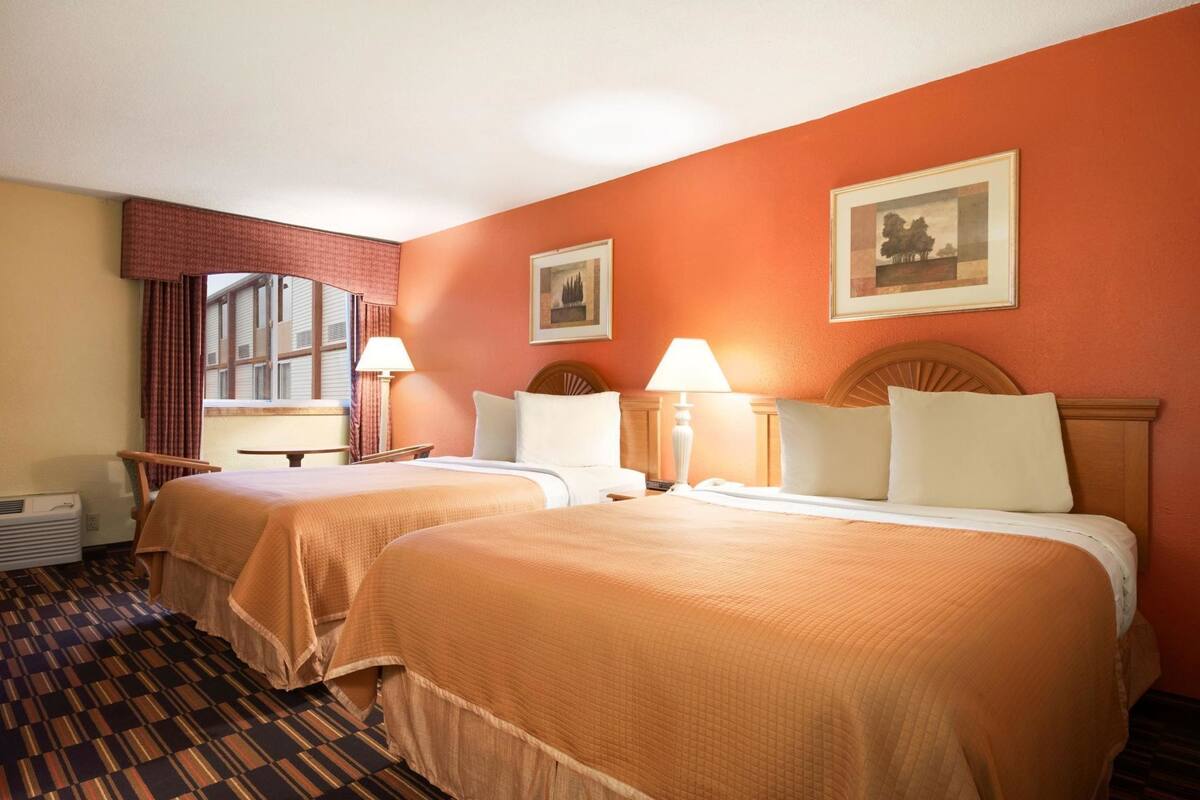 Habitación de hotel con dos camas, una ventana con cortinas, una mesa, una silla y un radiador.