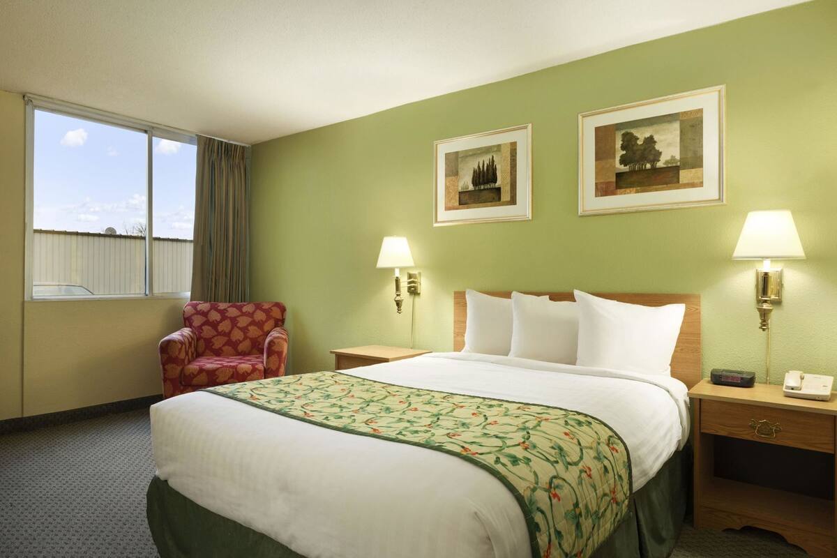 Una habitación de hotel con una cama, una silla, dos lámparas de pared y dos cuadros enmarcados.