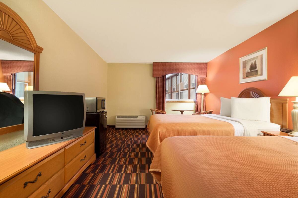 Habitación de hotel con dos camas, televisión, escritorio y ventana con cortinas.