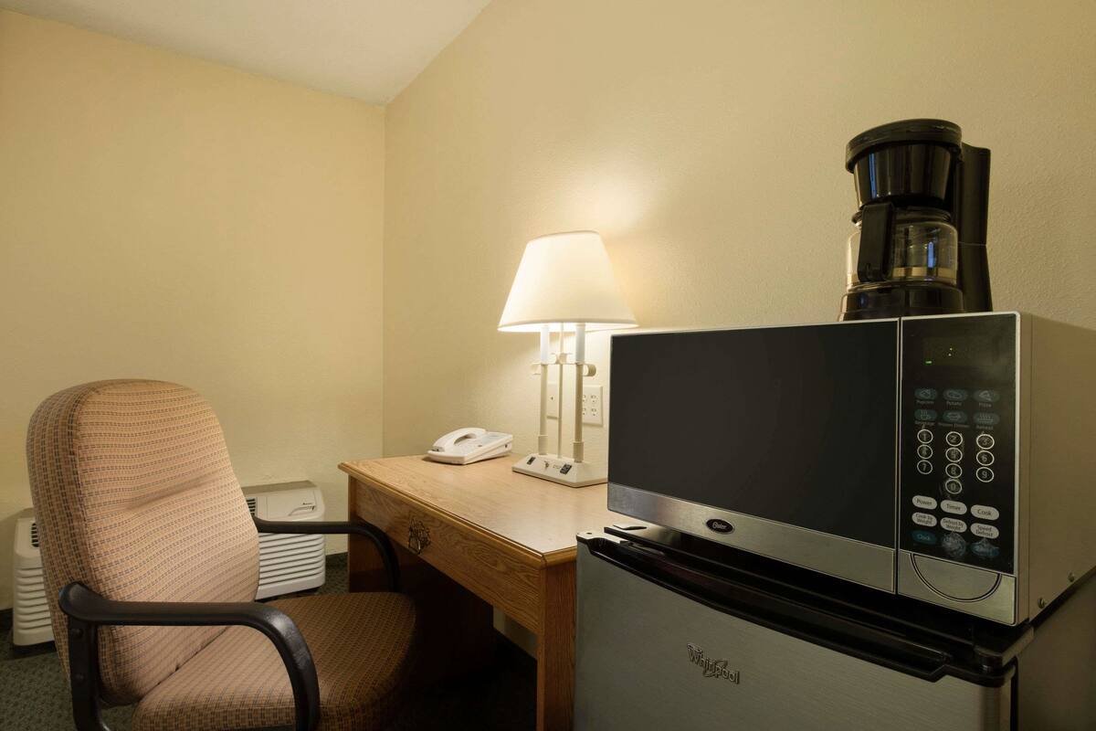 Habitación de hotel con microondas, cafetera, escritorio, silla y lámpara.