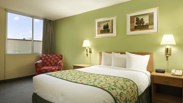 Une chambre d’hôtel avec un grand lit, deux lampes de chevet, une chaise et deux tableaux encadrés au mur.