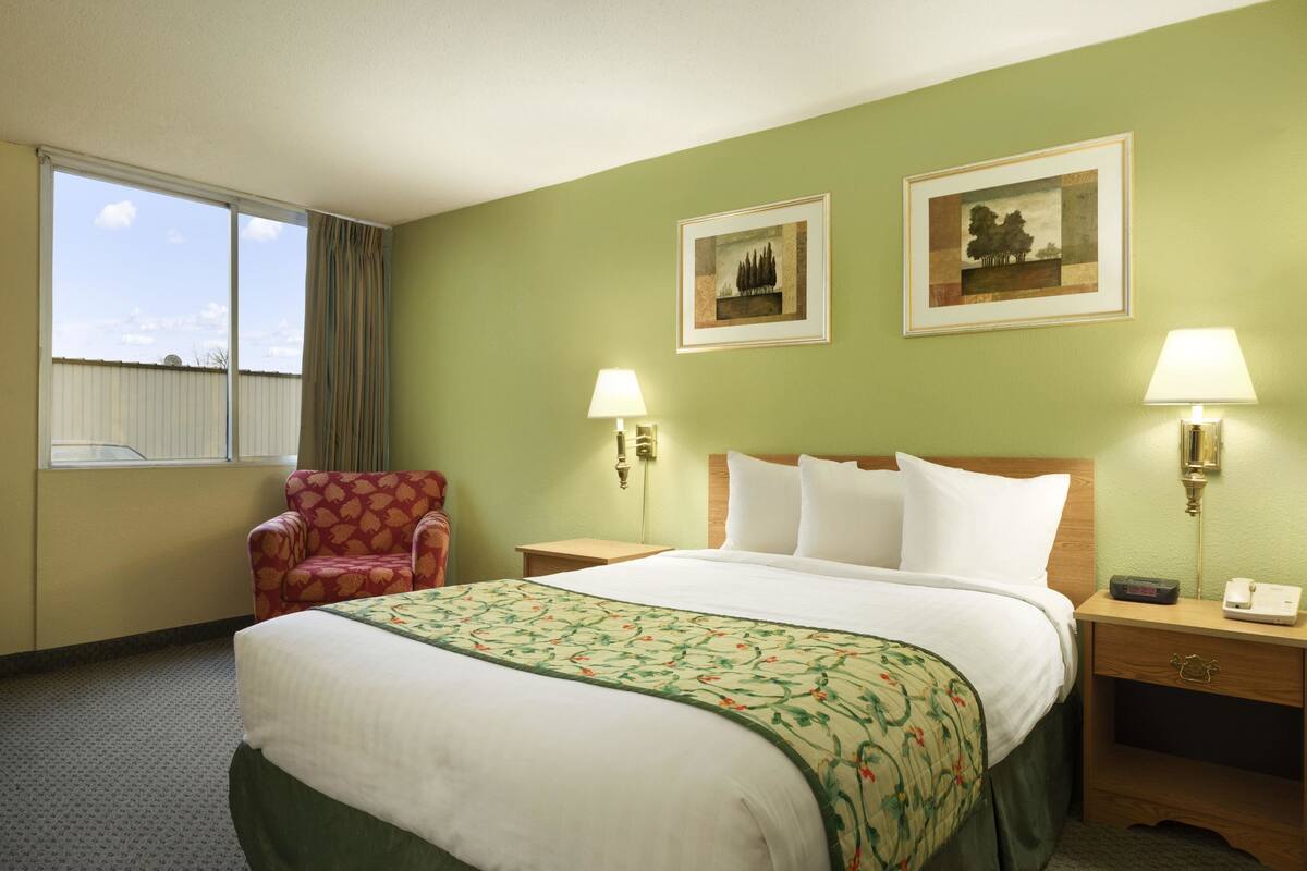 Una habitación de hotel con una cama grande, dos lámparas de noche, una silla y dos cuadros en la pared.